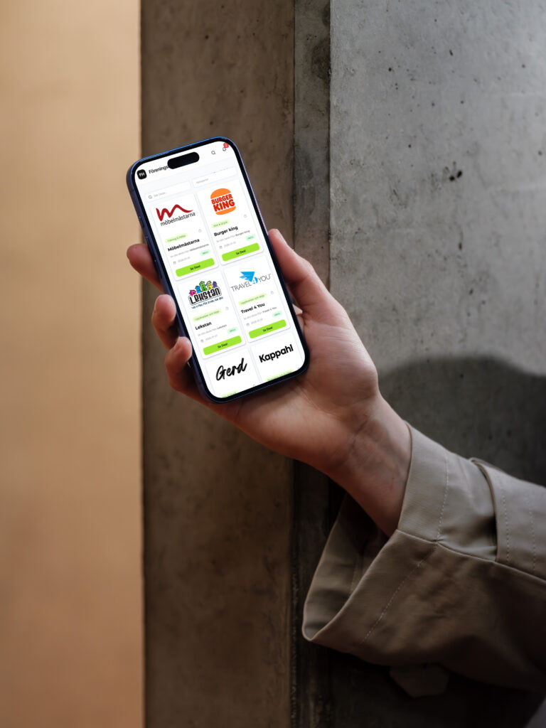 Hand som håller mobil med Föreningshäftets deals öppen mot en betongvägg.