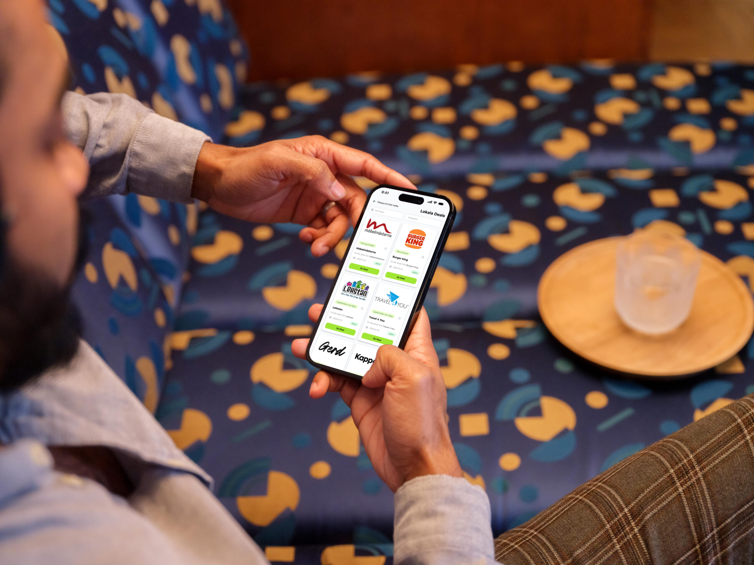 Person som sitter i en lounge och håller en iPhone som visar Föreningshäftets lista med tillgängliga deals.